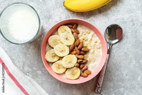 oatmeal with banana, almonds nuts in pink bowl, glass of milk, napkin on gray concrete background Top view Healthy breakfast or lunch Natural ingredients Rustic style