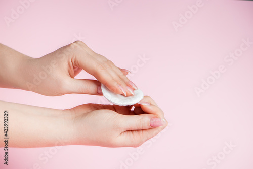 Hand care concept. Young woman remove nail polish on pink background. Place for text.