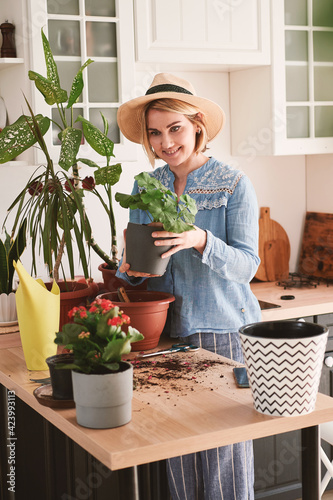 young woman in a straw hat growing and planting home flowers, at home