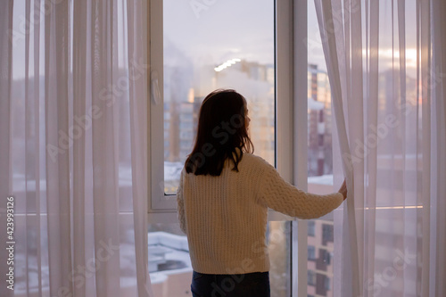 young beautiful woman in a white knitted sweater looks out the window at a city tea drinker