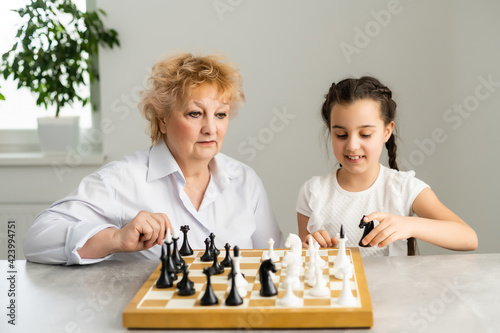 Happy girl with grandmother sitting at the table and playing chess