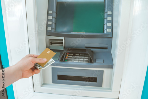 The guy holds money and a bank card in his hand in front of an ATM machine.