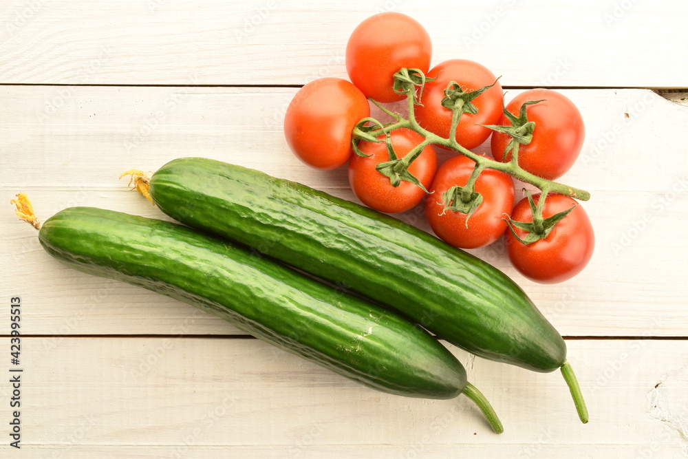 Several green cucumbers and red ripe, cocktail tomatoes on a twig, close-up, on a wooden table, top view. Several green cucumbers and red ripe, cocktail tomatoes on a twig, close-up, on a wooden table, top view.