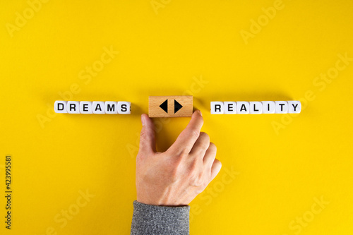 Hand holds a wooden cube with arrow icon between the options of dreams or reality. To chase the dreams or to face the reality dilemma. photo