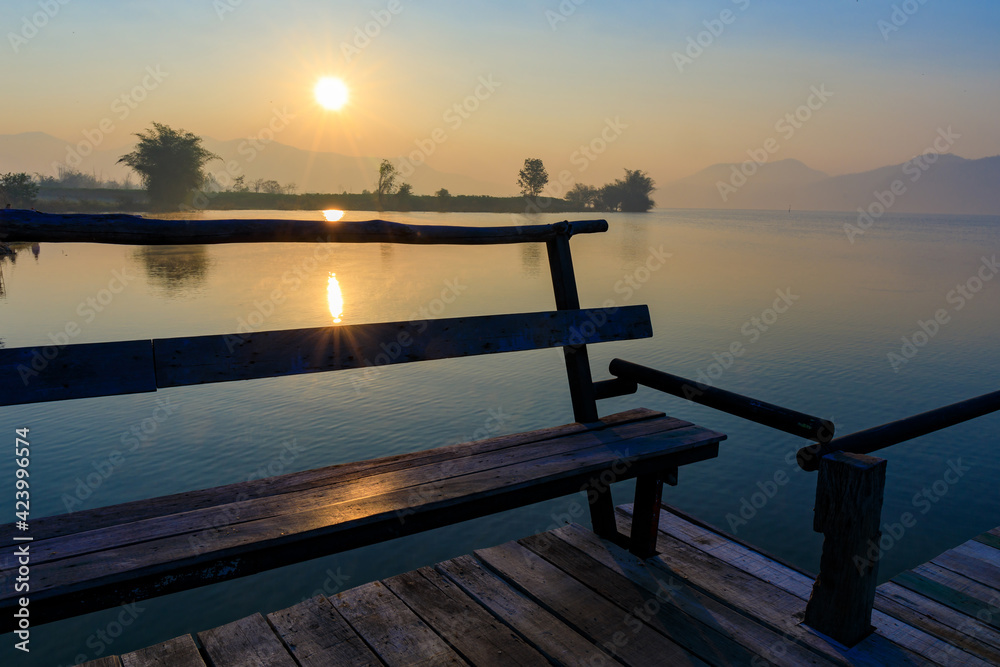 Wooden seat or bench on the wooden bridge on the lake with Sunrise time.
