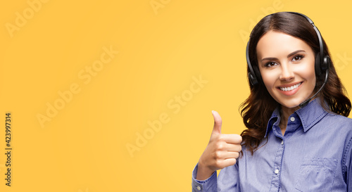 Contact Call Center Service. Customer support, female sales agent. Caller or answering phone operator or businesswoman in headset. Woman showing thumb up hand sign gesture. Yellow background with copy photo