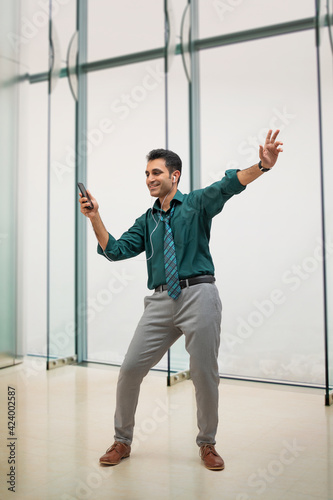 A HAPPY CORPORATE PROFESSIONAL DANCING WHILE HOLDING MOBILE PHONE 