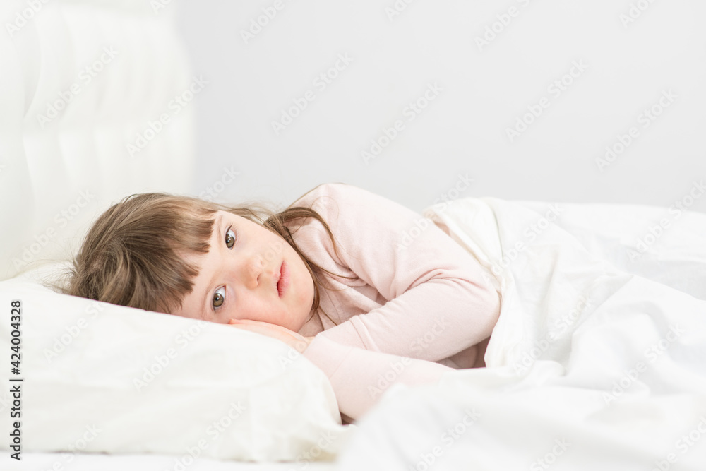 A girl with down syndrome lying on the bed under the covers and getting ready for bed. Usually childhood in a family for children with disabilities A girl with down syndrome lying on the bed under the covers and getting ready for bed. Usually childhood in a family for children with disabilities