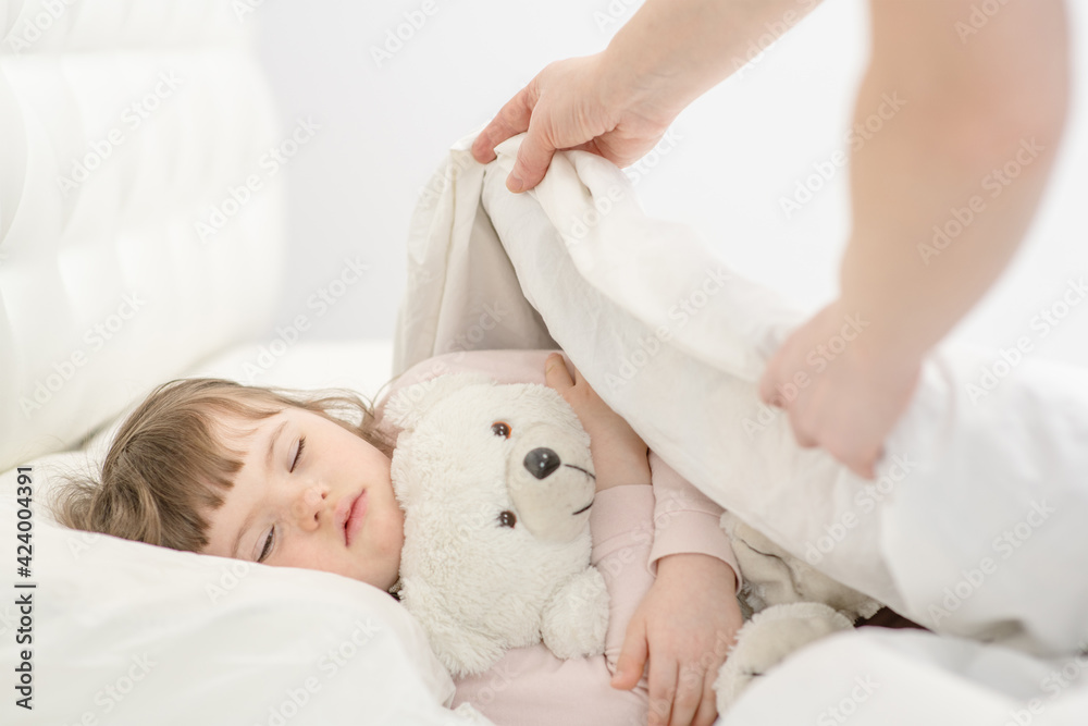 Mom covering a girl with down syndrome with a blanket. Ordinary childcare in a family for children with disabilities Mom covering a girl with down syndrome with a blanket. Ordinary childcare in a family for children with disabilities