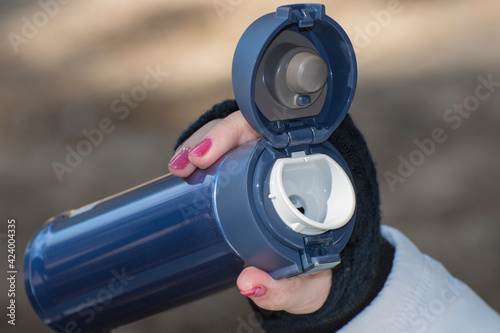 The girl is holding a coffee mug open for drinking. The use of thermal dishes during a hike or travel. Family weekend in nature.