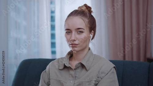 Portrait young woman with headphones look at camera sitting on sofa. Confident, enjoying, joyful, relaxed, indoors, beauty, feminine, female, adult, attractive. Slow motion