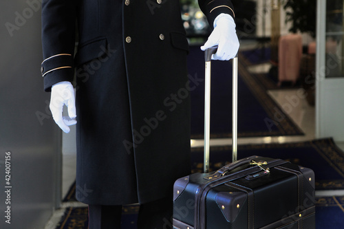 The doorman is holding a suitcase. Uniform and white gloves on the doorman.An unrecognizable person. Free space.Concept of hotel service