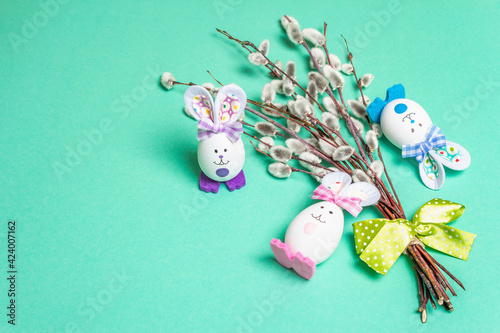 Sprig of willow isolated on pastel turquoise background with handmade funny bunnies from the egg