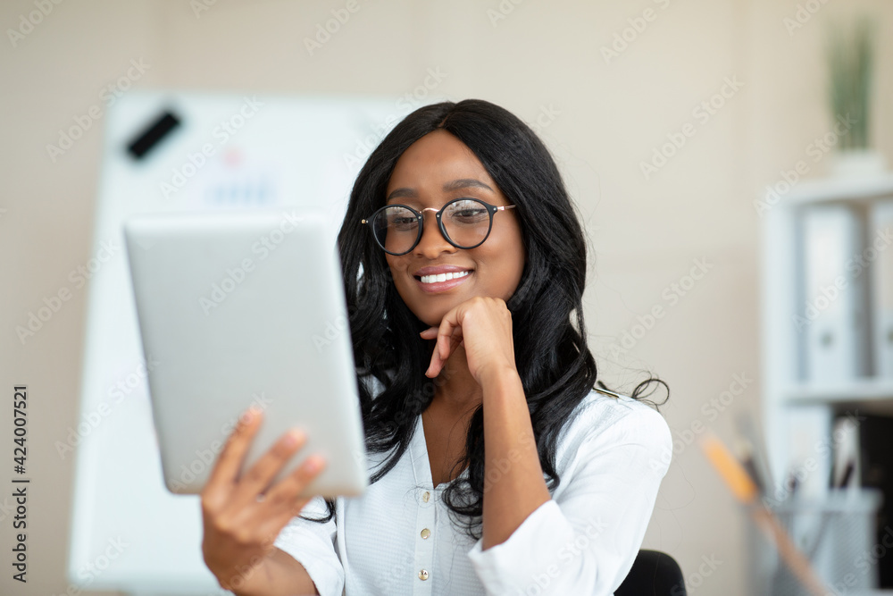 Portrait of happy black businesswoman using tablet computer, making video call, chatting online with colleague in office