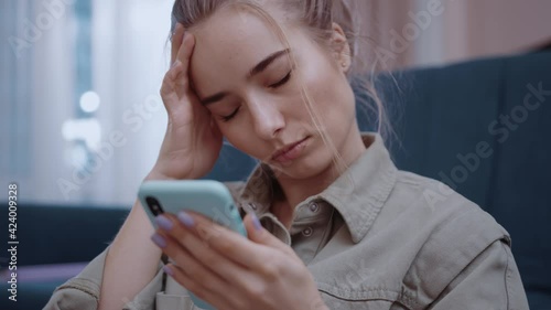 Close up young woman use phone sitting in home near sofa feel sick unhappy headache. Attractive, online, mobile, tired, cellphone, application, smartphone, internet. Slow motion