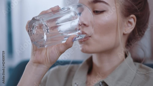 Close up hands woman hold drink water sitting on sofa at home. Glass, relaxed, morning, enjoying, apartment. Portrait. Slow motion
