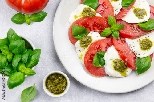 Traditional italian caprese salad with sliced tomatoes, mozzarella, basil, pesto sauce and spice on a light background. Top view. Close up.