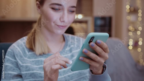 Face young woman use phone at home feel relax happy sitting on sofa in modern room at evening. Social media, girl, technology, mobile, online, typing, business, communication. Slow motion