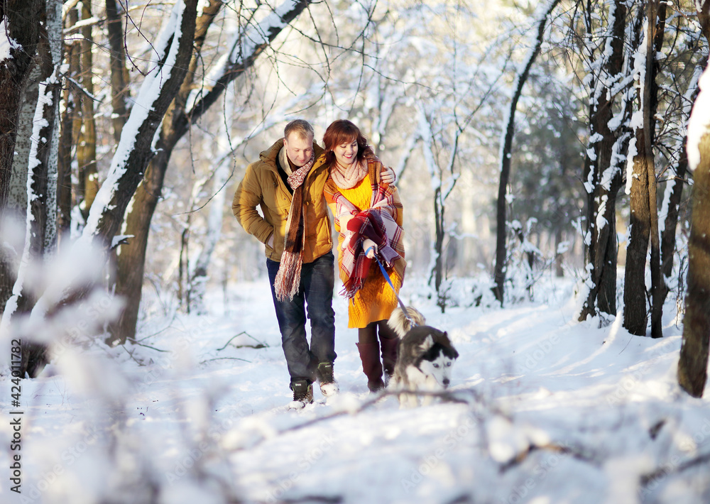 Fototapeta premium Young couple smiling and having fun in winter park with their husky dog