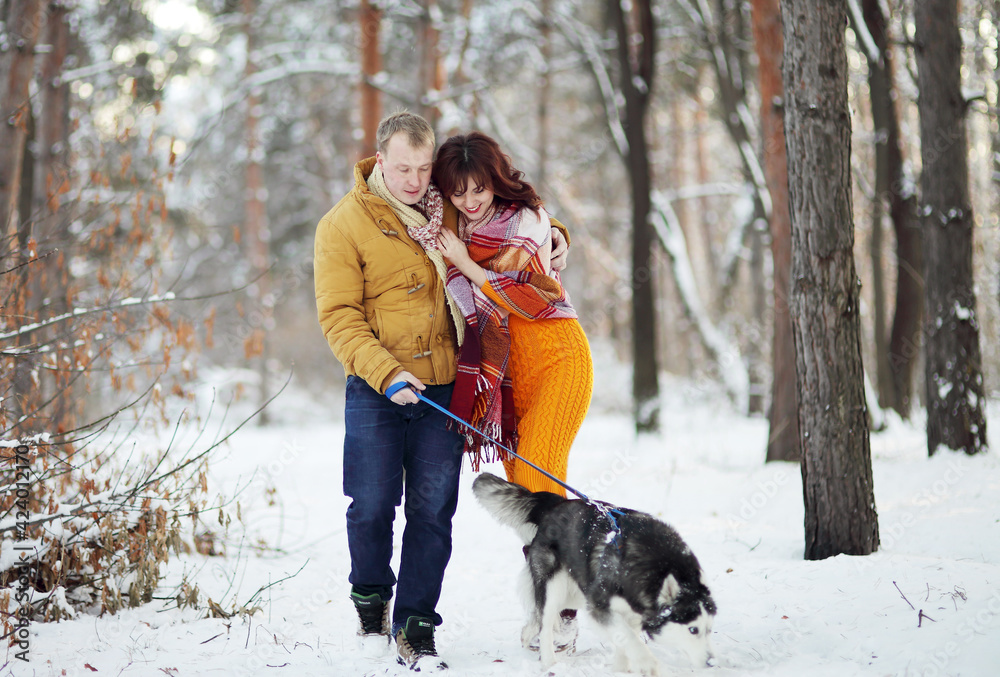 Young couple smiling and having fun in winter park with their husky dog Young couple smiling and having fun in winter park with their husky dog
