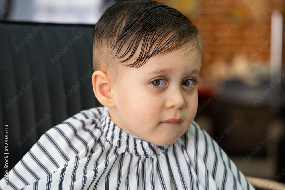 Barber in barbershop cuts hair happy child boy. Lifestyle close-up. Concept of beauty, hygiene and care salon Barber in barbershop cuts hair happy child boy. Lifestyle close-up. Concept of beauty, hygiene and care salon