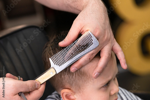 Barber in barbershop cuts hair happy child boy. Lifestyle close-up. Concept of beauty, hygiene and care salon