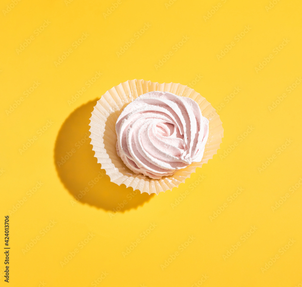 On a yellow background lies a pink marshmallow with a hard shadow. Blank for the pattern. Selective focus. On a yellow background lies a pink marshmallow with a hard shadow. Blank for the pattern. Selective focus.