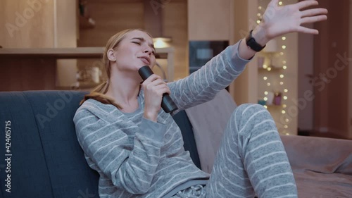 Funny young woman singing television karaoke sitting on sofa in apartment. Use tv remote, enjoyment, smiling, happiness, attractive, adult, entertainment. Close up . Slow motion