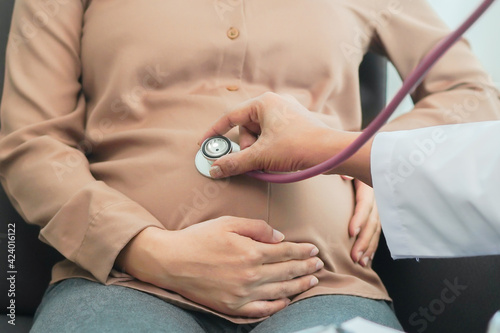 Doctor using stethoscope listening baby in pregnant belly at clinic / hospital photo