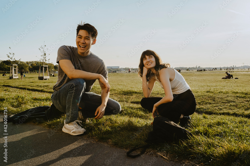 Happy friends crouching on grass against sky in park Happy friends crouching on grass against sky in park