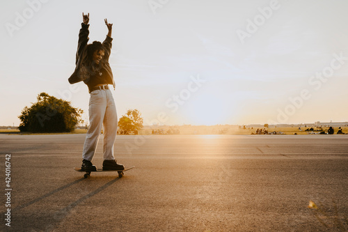 Cheerful woman with hand raised skating on road in park