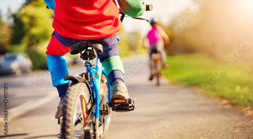 Fototapeta Naklejka Na Ścianę i Meble -  Cute children riding on bicycles on asphalt road in summer.