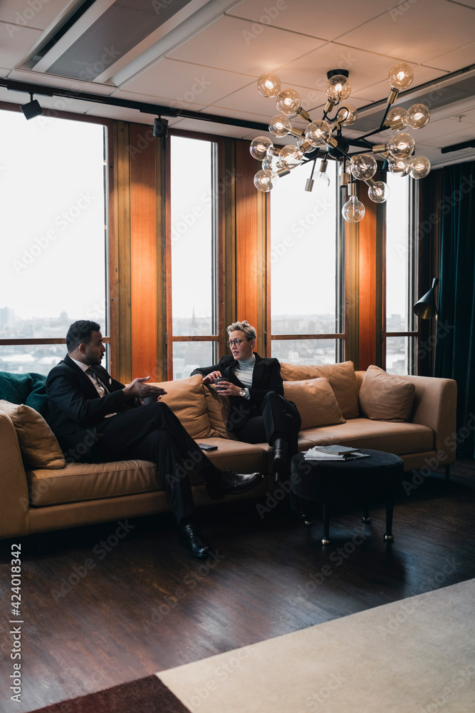 Male and female colleagues discussing strategy while sitting on sofa in office Male and female colleagues discussing strategy while sitting on sofa in office