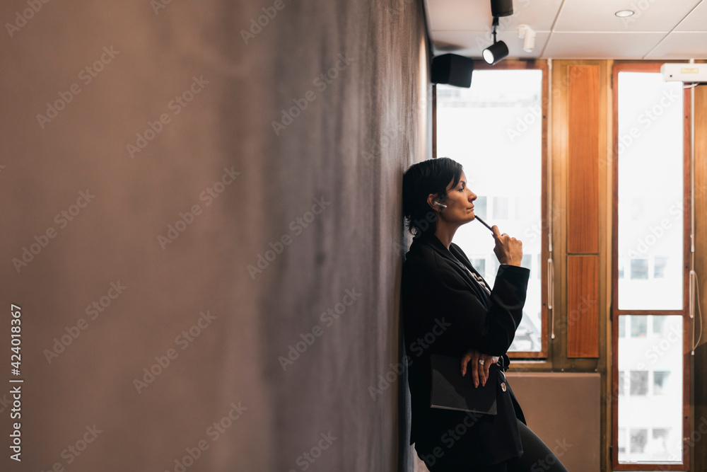 Thoughtful mature female entrepreneur leaning on wall at office Thoughtful mature female entrepreneur leaning on wall at office