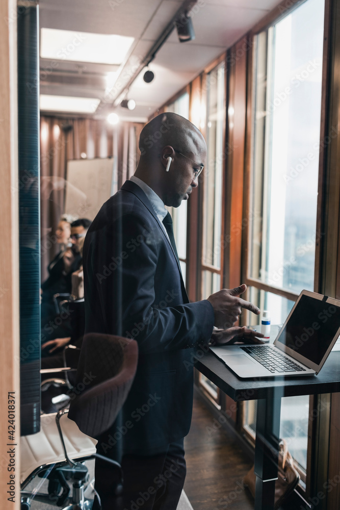 Side view of bald male entrepreneur using laptop in board room seen through glass wall Side view of bald male entrepreneur using laptop in board room seen through glass wall