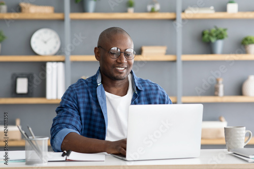 Freelance career. African american man working on laptop computer, doing new project, sitting at home workplace