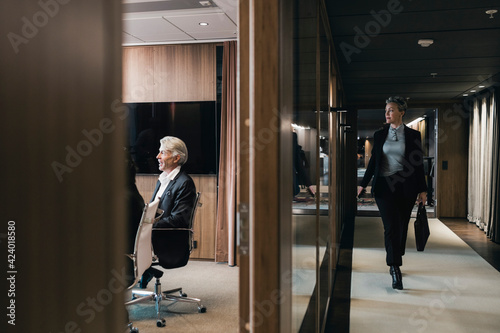 Full length of businesswoman walking in corridor while looking at board room