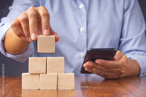 Hand holding a smartphone and blank wooden blocks while sitting on a chair. Close-up photo. Space for text photo