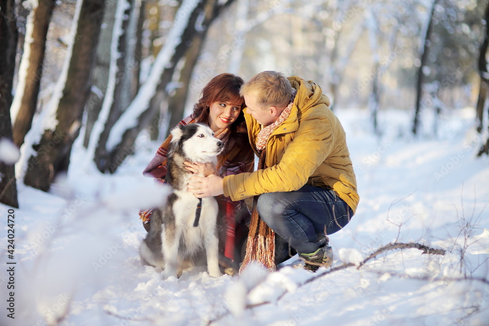 Couple smiling and having fun in winter park with their husky dog Couple smiling and having fun in winter park with their husky dog