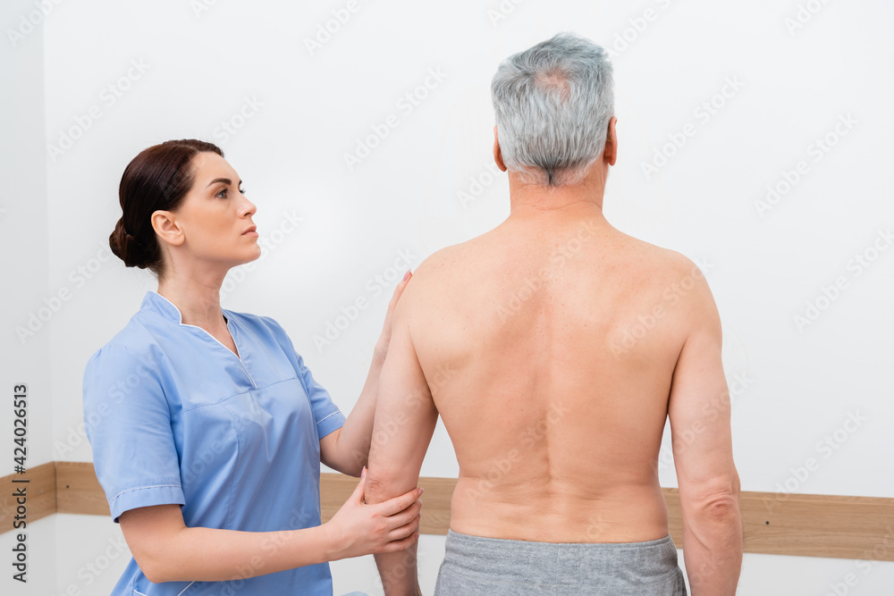 attentive orthopedist examining shirtless man in rehabilitation center attentive orthopedist examining shirtless man in rehabilitation center