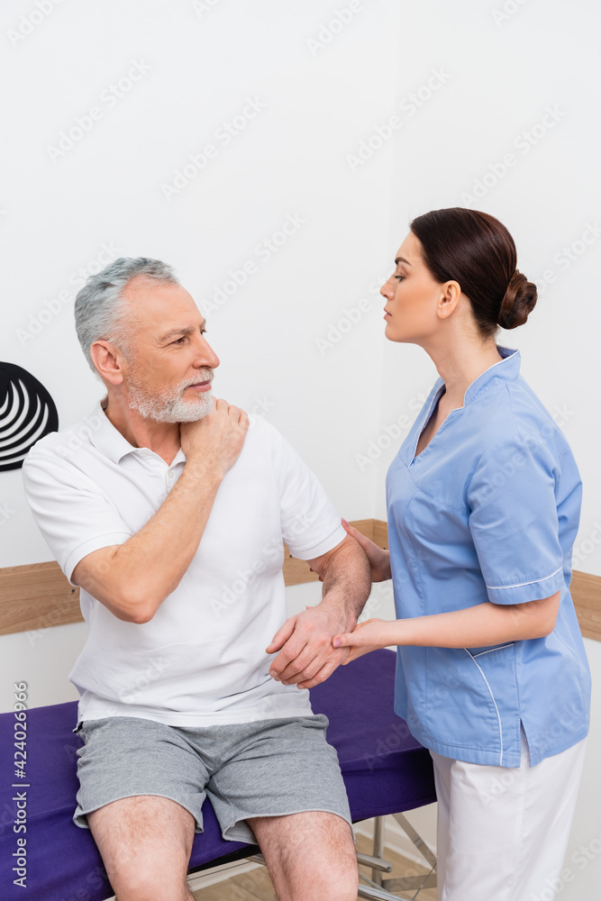 Obraz premium mature man touching shoulder during consultation with rehabilitologist