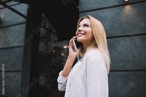 Happy young female having phone call while looking up in city street