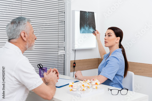brunette rehabilitologist showing x-ray to mature man during consultation