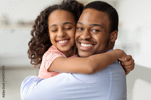 Emotional african american school girl hugging her cheerful dad
