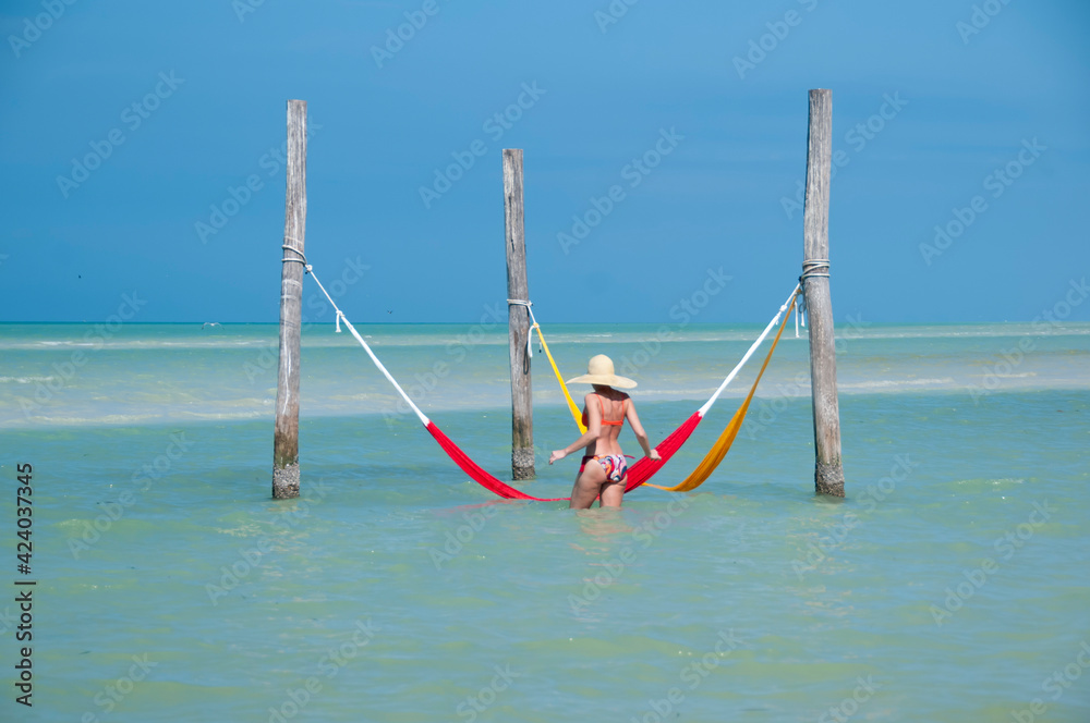 A young woman with a sombrero relaxes in a hammock over the sea in Holbox Island, Mexico. In the background the blue sky and the Caribbean Sea. Concept travel and tourism A young woman with a sombrero relaxes in a hammock over the sea in Holbox Island, Mexico. In the background the blue sky and the Caribbean Sea. Concept travel and tourism