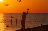 A young girl by the Caribbean Sea, with one arm, raised, playing with seagulls, the island of Holbox Mexico. A happy girl at sunset. Concept travel tourism