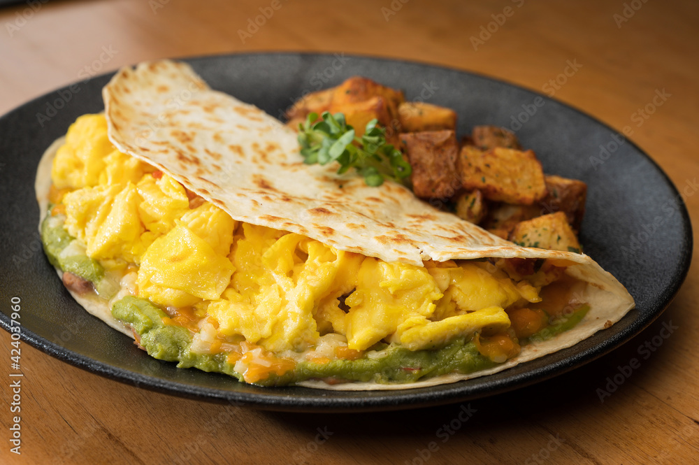 Huevos Rancheros.  Three scrambled eggs in a flour tortilla with refried beans, guacamole and shredded cheese.