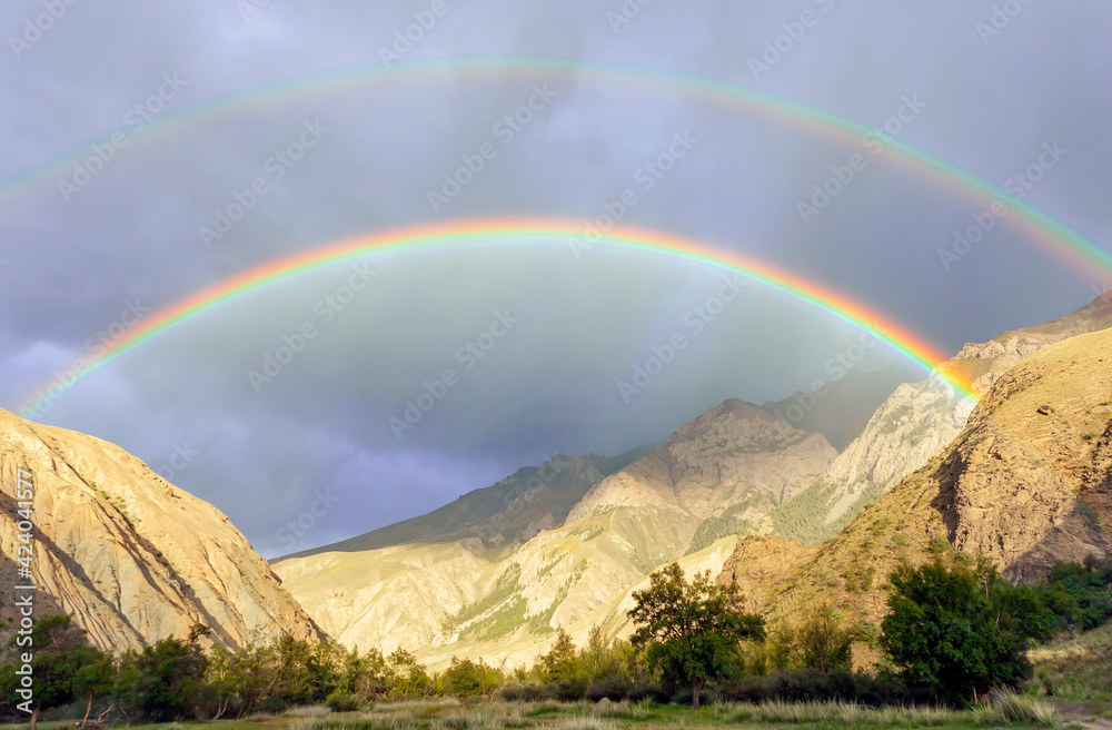 Double rainbow and heavy rain over the mountain valley.