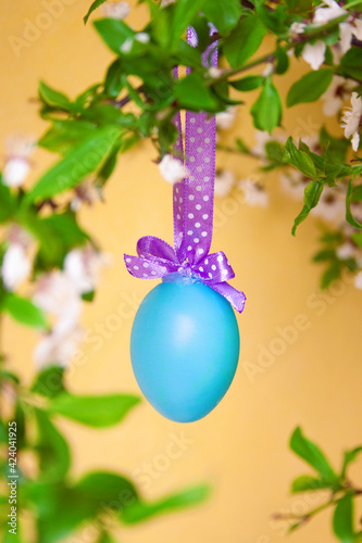 A painted Easter egg hung on a ribbon on a branch of blossoms