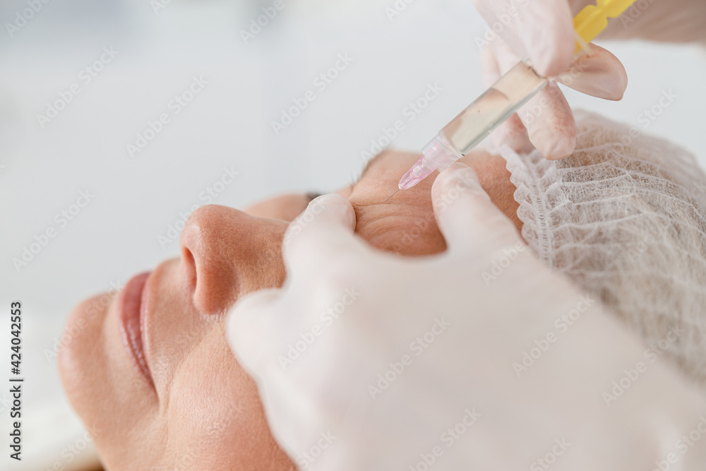 Naklejka premium Close up makes mesotherapy injections to a senior woman. Treatment of a woman by a beautician for tightening and smoothing wrinkles on the face skin